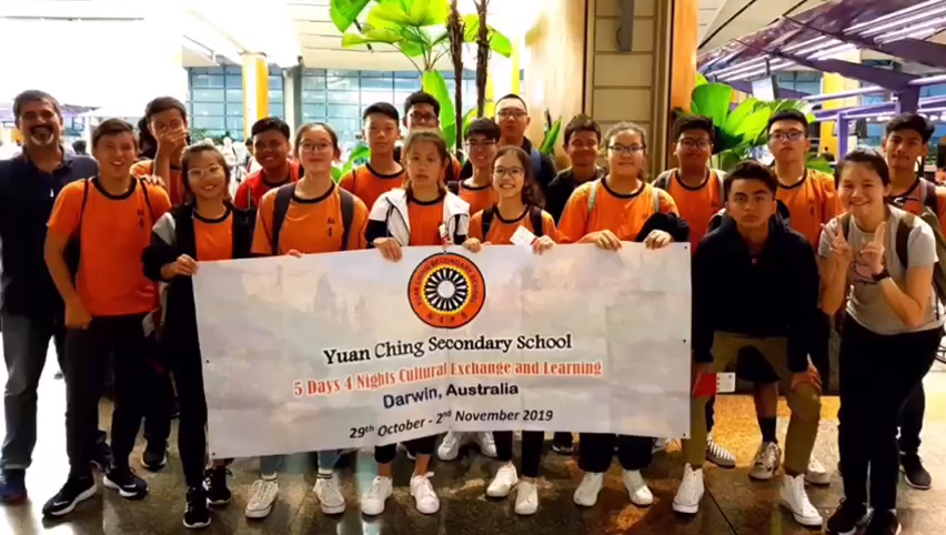 Copilot said: Group photo of Yuan Ching Secondary School students and accompanying adults holding a programme banner during a cultural exchange and learning trip to Darwin, Australia.